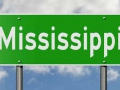 Green highway sign with clouds in the background showing the state Mississippi